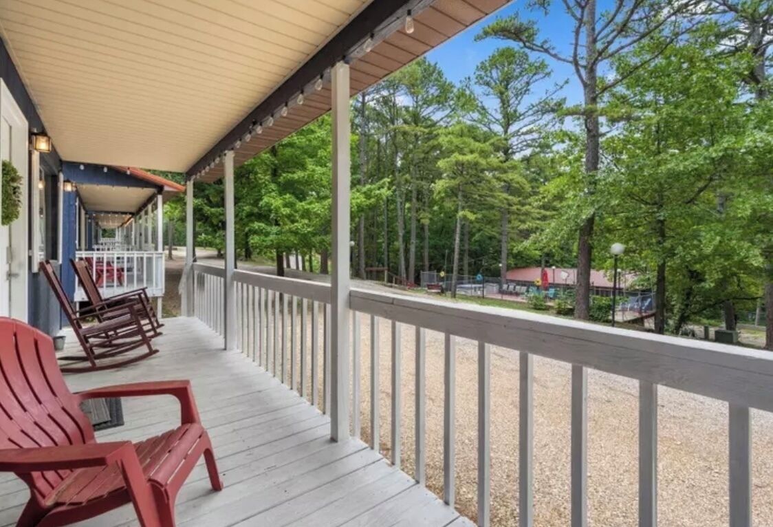 Une véranda couverte avec une balustrade, des fauteuils Adirondack rouges et une vue sur une zone boisée.
