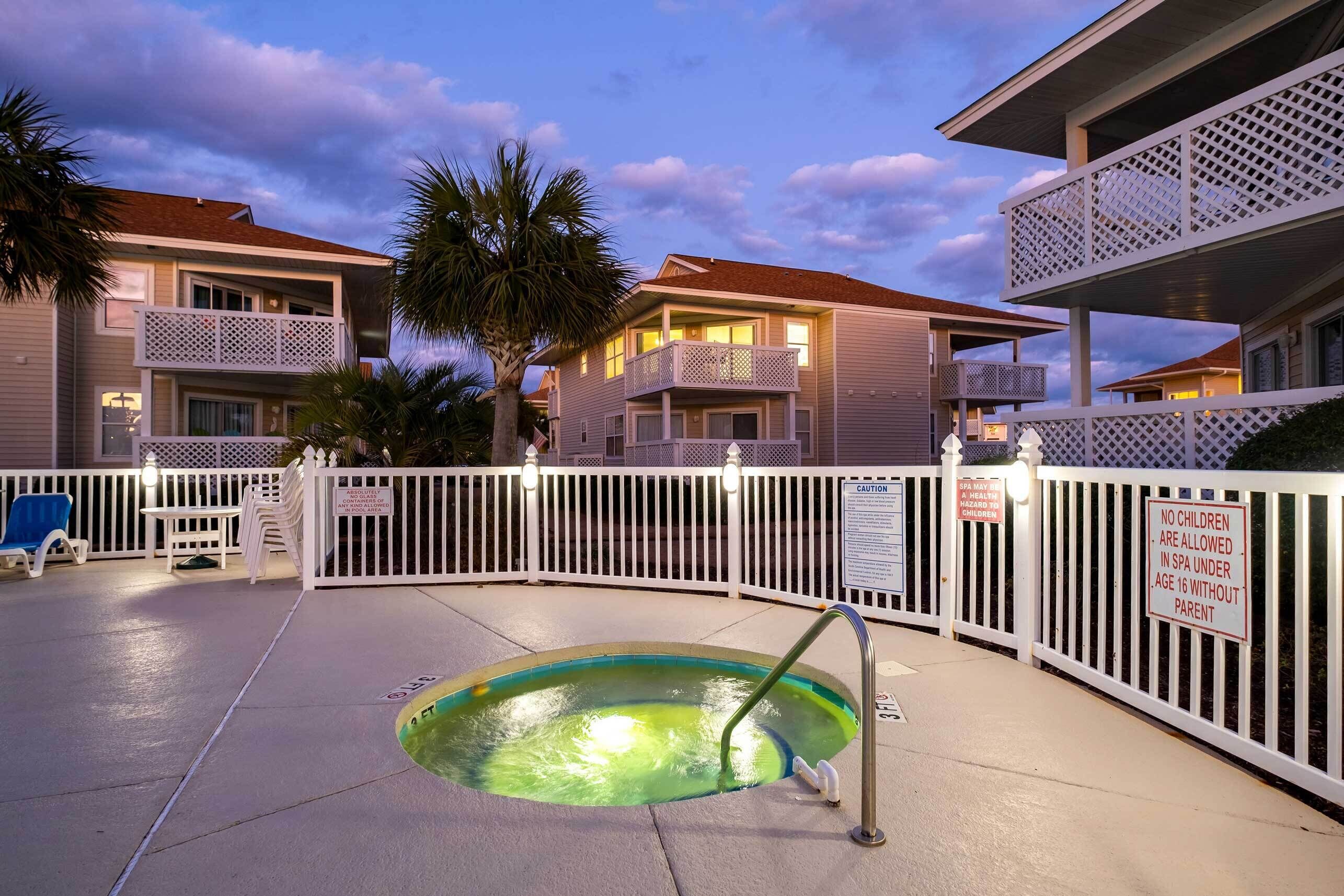 A swimming pool with a metal ladder, surrounded by a white fence with caution signs, and a palm tree in the background.