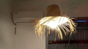 Una habitación con ventilador de techo, aire acondicionado, ventana con vista a una estructura de madera y una lámpara fijada a la pared.