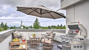 Un patio exterior con una parrilla, muebles de mimbre y una mesa con fruta y bebidas.
