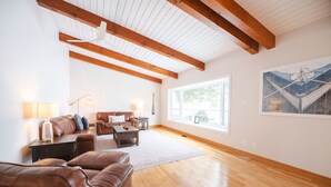 A spacious living room with a high ceiling, wooden beams, a large window, and a painting on the wall. - Breathtaking 5 bedroom Waterfront Home With Hot Tub! (Port McNicoll)