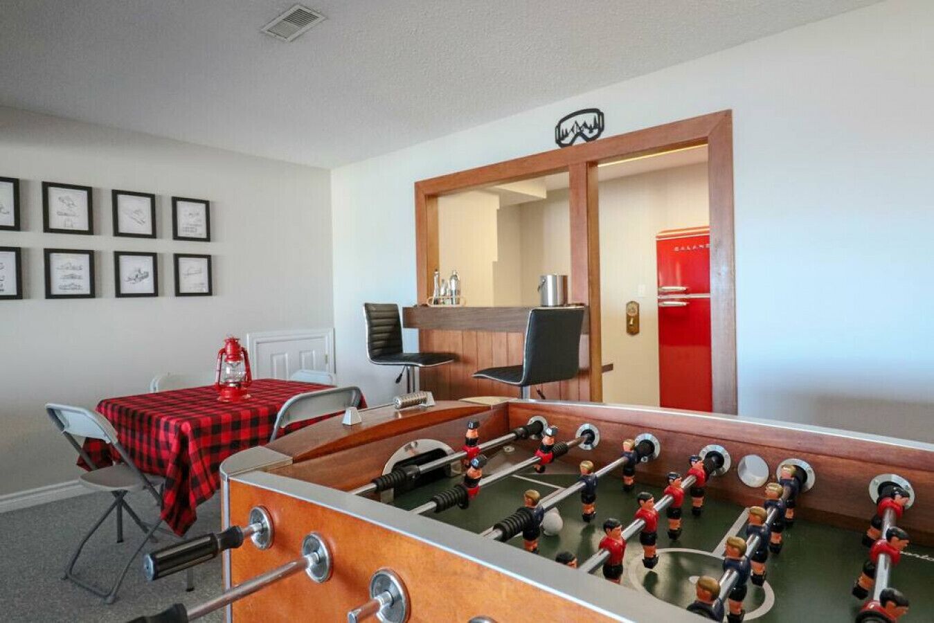 Una habitación con mesa de fútbol, mantel a cuadros rojo y negro, y cuadros en la pared.