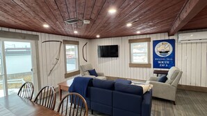 Ein gemütliches Zimmer mit Holzwänden, einem blauen Sofa, einem Esstisch mit Stühlen und einem an der Wand befestigten Fernseher.