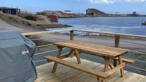 Ein Holztisch mit Grillabdeckung auf einer Holzterrasse, angrenzend an ein Gewässer.