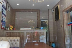Un vestíbulo de hotel con una mesa de recepción, un área de estar con un sofá de cuero capitonado y una amplia mesa de conferencias de madera.