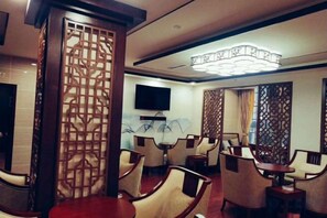 Habitación de hotel con zona de comedor, televisor montado en la pared y un biombo decorativo.