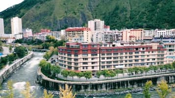 A multi-story hotel with a river in the foreground, surrounded by greenery and hills.