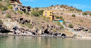 A coastal villa with a view of the sea, a rocky hillside, and a clear sky.