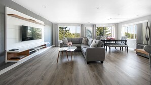 A modern living room with a grey sofa, a glass coffee table, and a flat-screen TV mounted on a white wall. - High Point Guesthouse (Seattle)