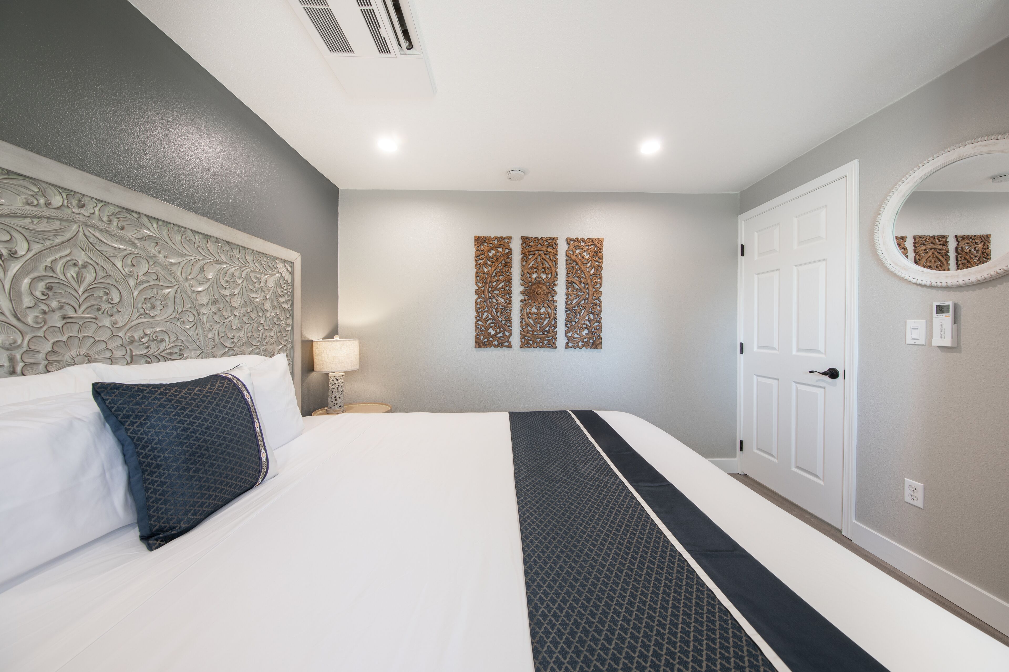 Una habitación de hotel con una cama grande, un cabecero decorativo, un espejo montado en la pared y una puerta.