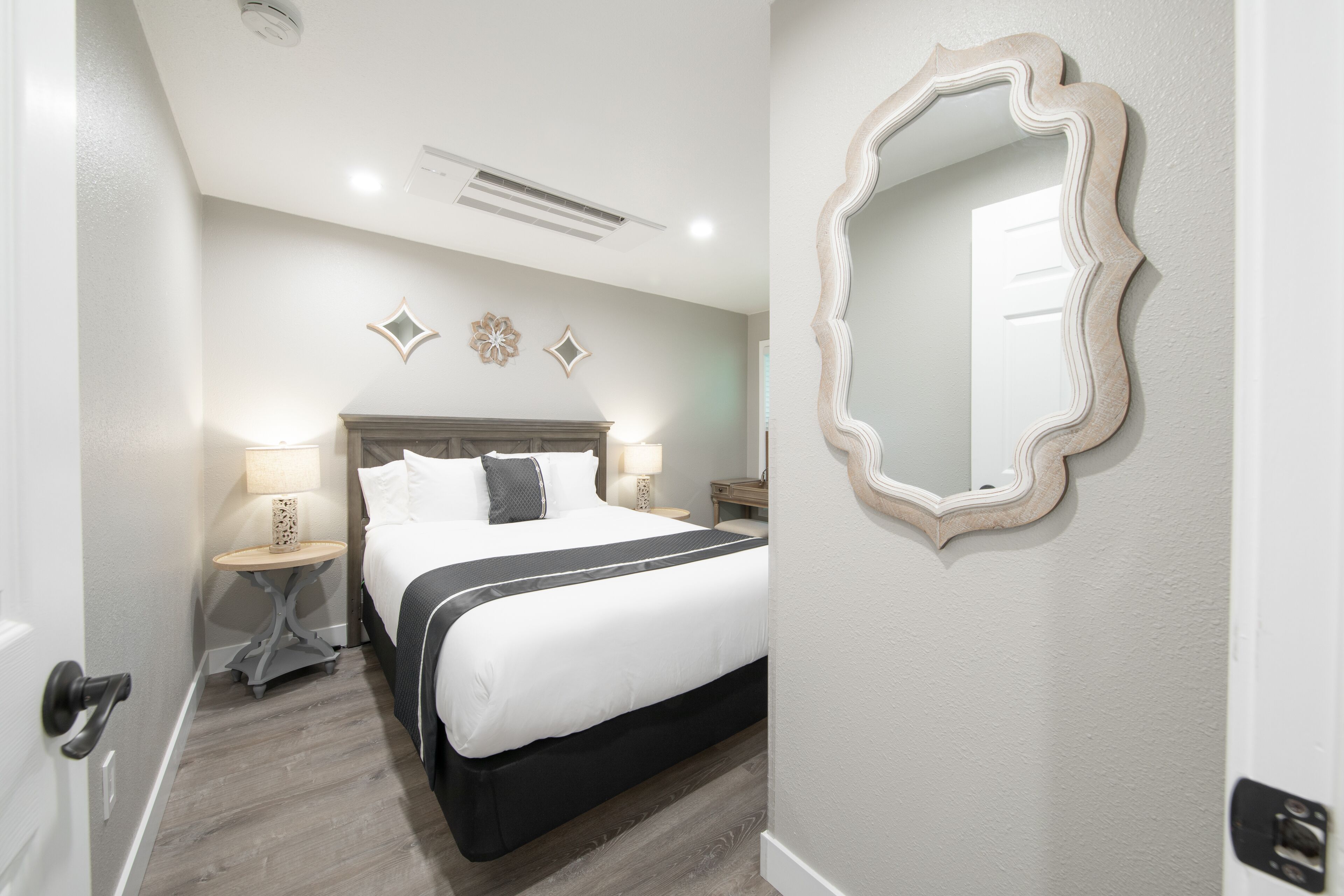 Een hotelkamer met een bed, nachtkastjes, een spiegel en decoratieve wandpanelen.