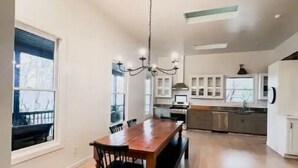 A spacious kitchen with a wooden dining table and chairs, a chandelier, and a view of the outdoors through large windows. - Luxurious 3-BR Home: BBQ Grill, Hot Tub & Fire Pit (Angels Camp)