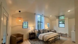 A spacious bedroom with a large bed, a sitting area with a chair, and a window providing natural light. - Luxurious 3-BR Home: BBQ Grill, Hot Tub & Fire Pit (Angels Camp)