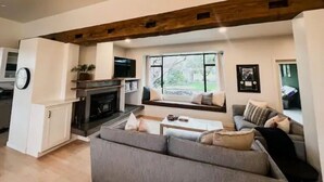 A spacious living room with a fireplace, a large window, and a cozy seating area. - Luxurious 3-BR Home: BBQ Grill, Hot Tub & Fire Pit (Angels Camp)