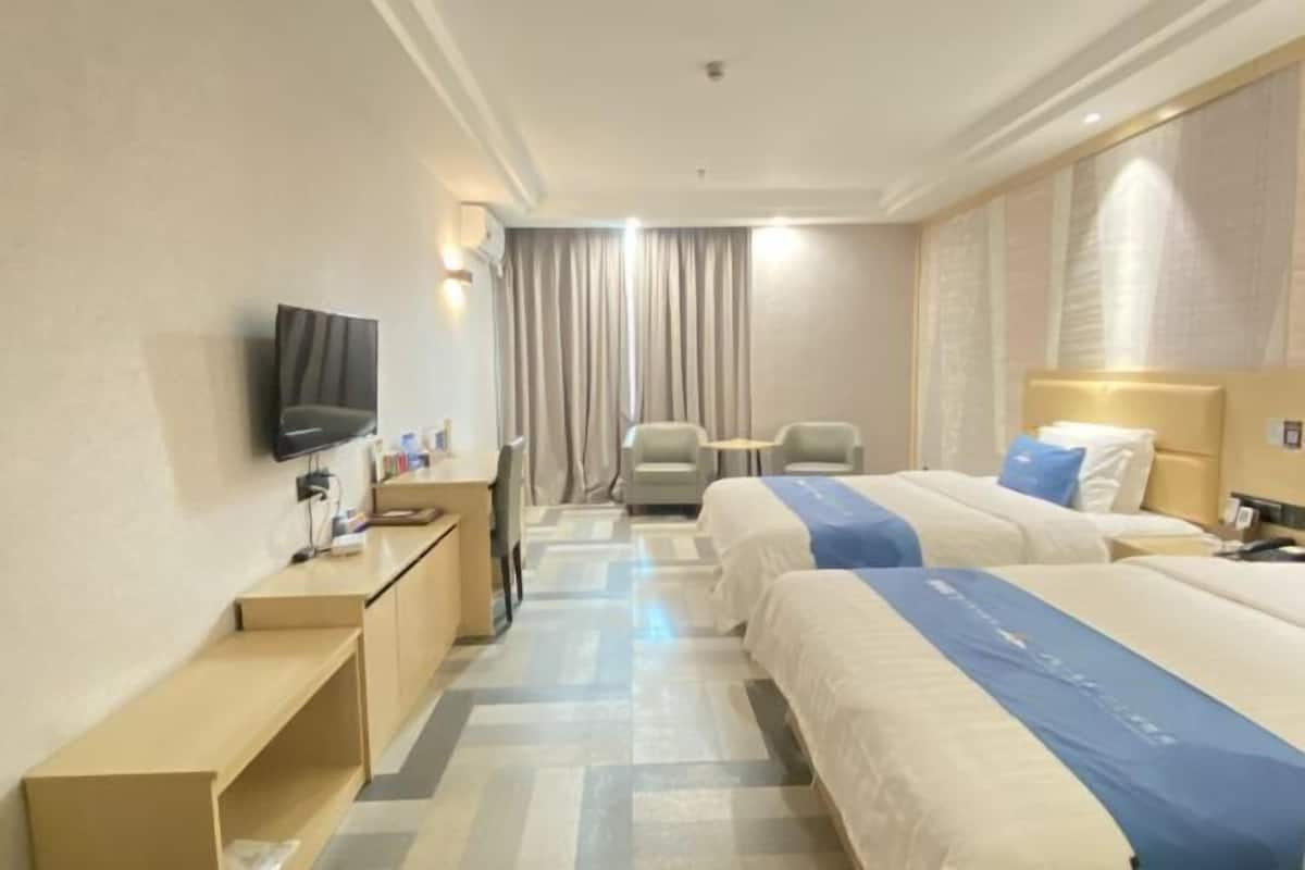 Habitación de hotel con dos camas, un escritorio, una silla, un televisor y una cortina.