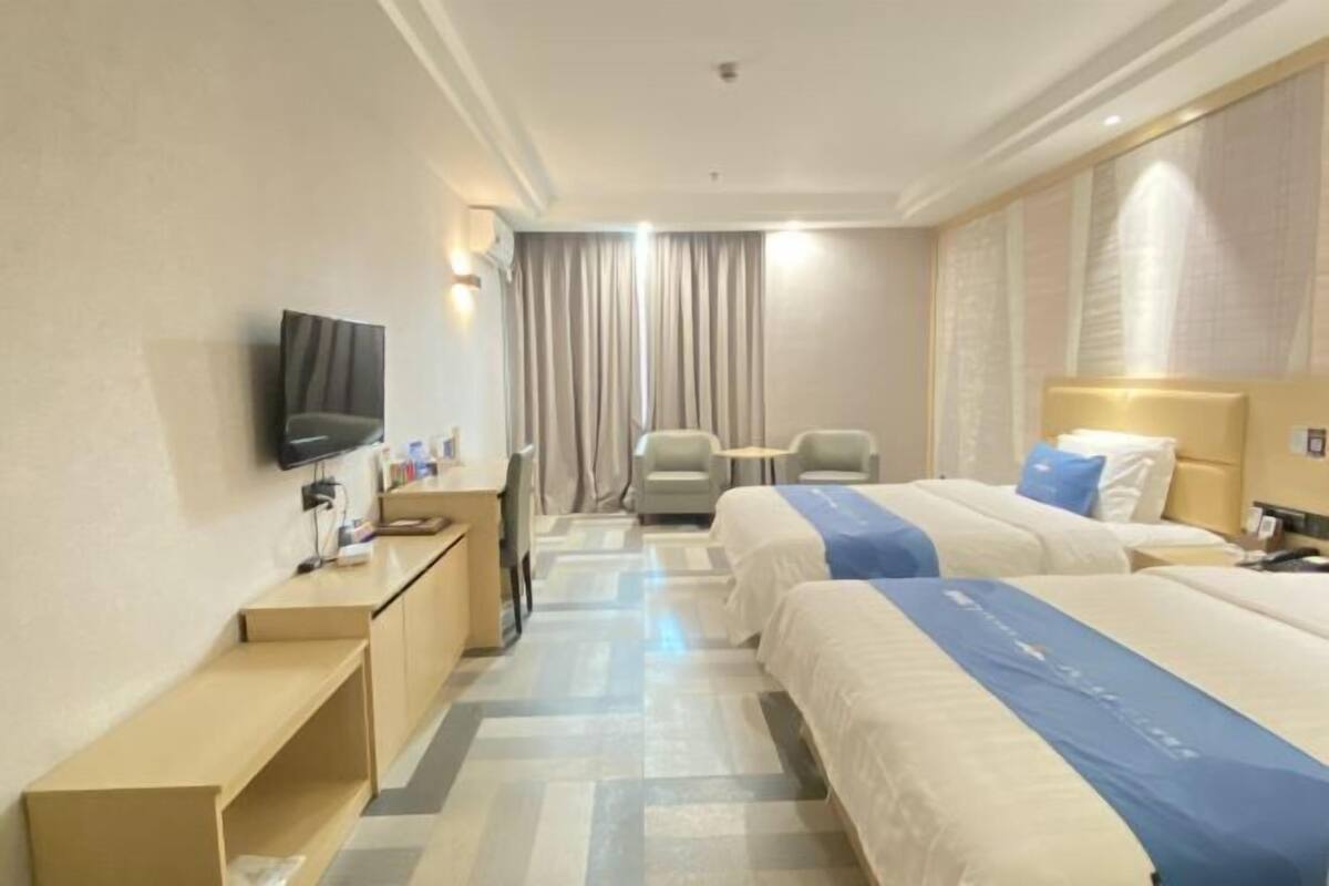 Hotellihuone, jossa on kaksi sänkyä, työpöytä, tuoli, televisio ja verho.