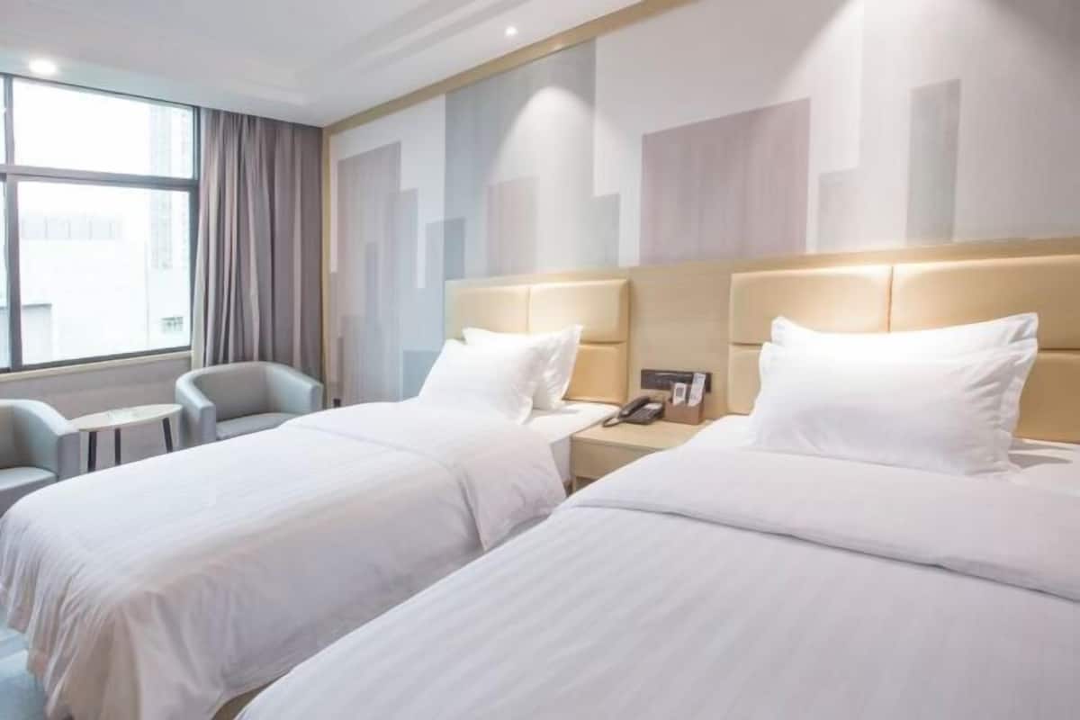 Habitación de hotel con dos camas, una mesita, una silla y una ventana con cortinas.