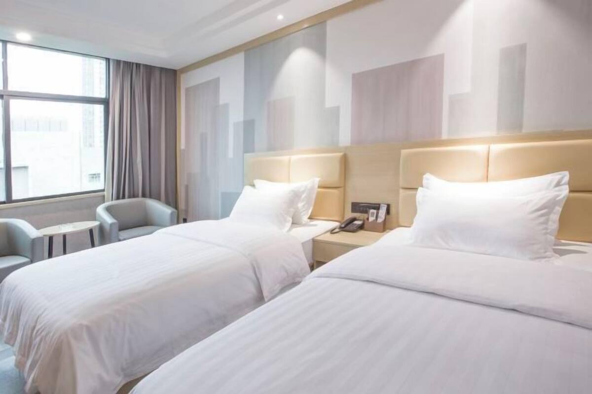 Hotellihuone, jossa on kaksi sänkyä, pieni pöytä, tuoli ja ikkuna, jossa on verhot.