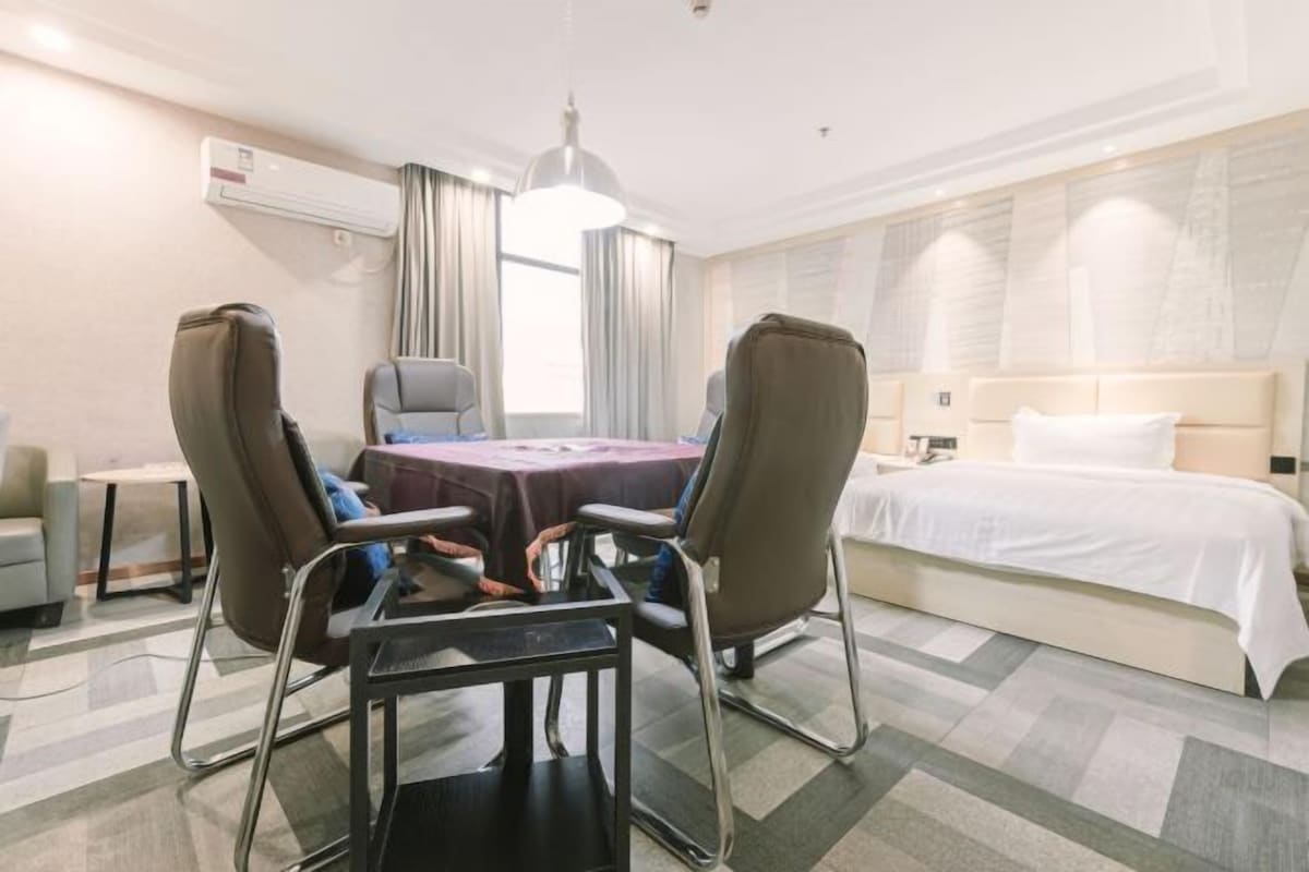 Une chambre d’hôtel comprenant un lit, un bureau avec deux chaises, une table et une grande fenêtre avec des rideaux.