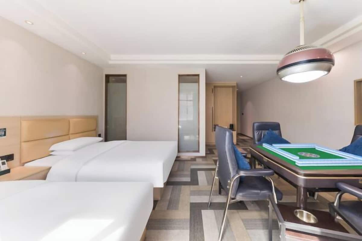 Una habitación de hotel con dos camas, un escritorio con una mesa verde y una lámpara colgante moderna.