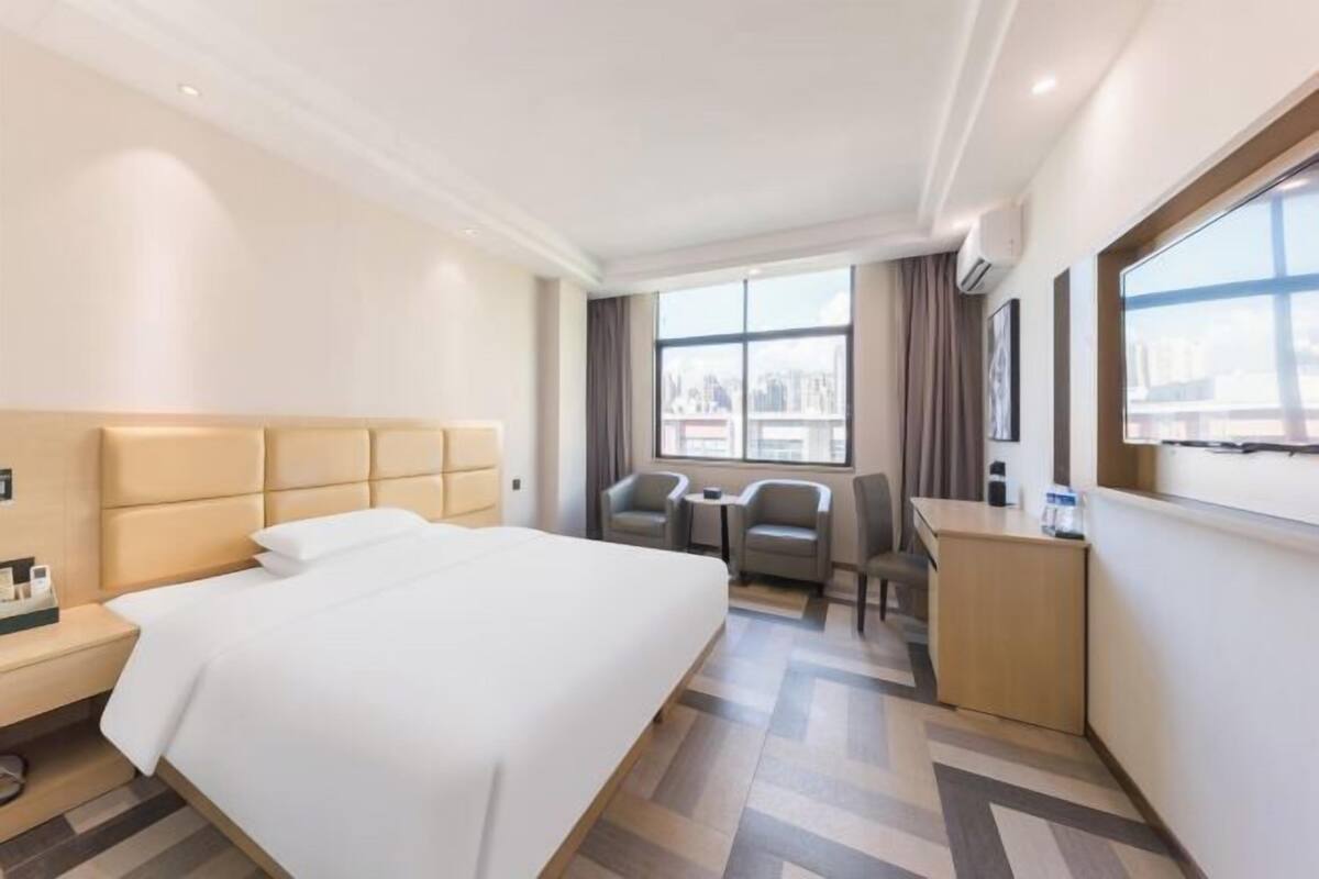 Una habitación de hotel con una cama, dos sillones, una mesita, un escritorio y un ventanal grande.