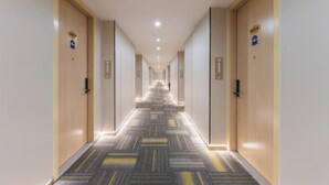 Un pasillo de hotel con piso alfombrado, puertas de madera e iluminación empotrada en el techo.