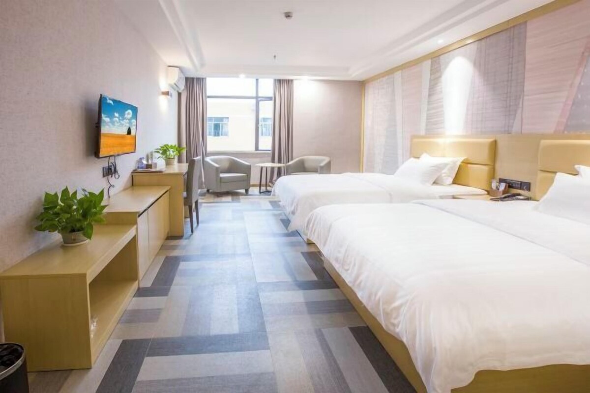 Une chambre d’hôtel avec deux lits, un bureau, une chaise, une télévision et une fenêtre avec des rideaux.