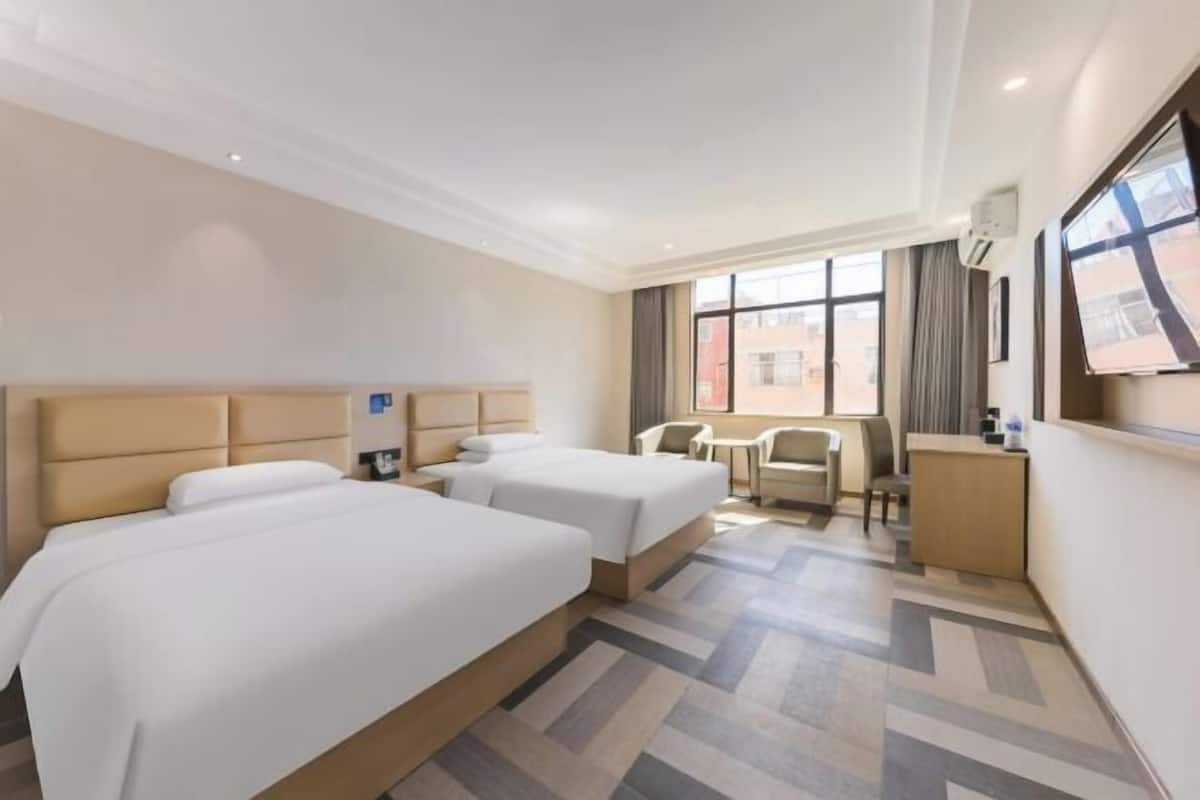 Habitación de hotel con dos camas, un escritorio, una silla y un ventanal grande.