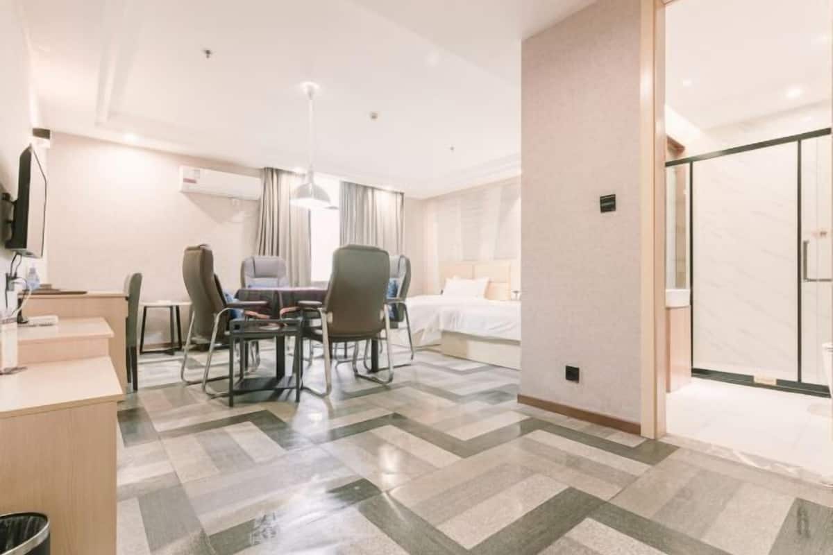Habitación de hotel con mostrador de recepción, zona de comedor con sillas, cama y zona de ducha.