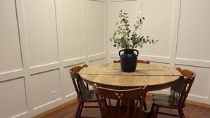 A round wooden dining table with a black vase of green plants in the center, surrounded by wooden chairs. - Unique apartment in historic downtown (Vandalia)