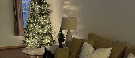 A living room with a Christmas tree, a sofa, a lamp, and a window with curtains.