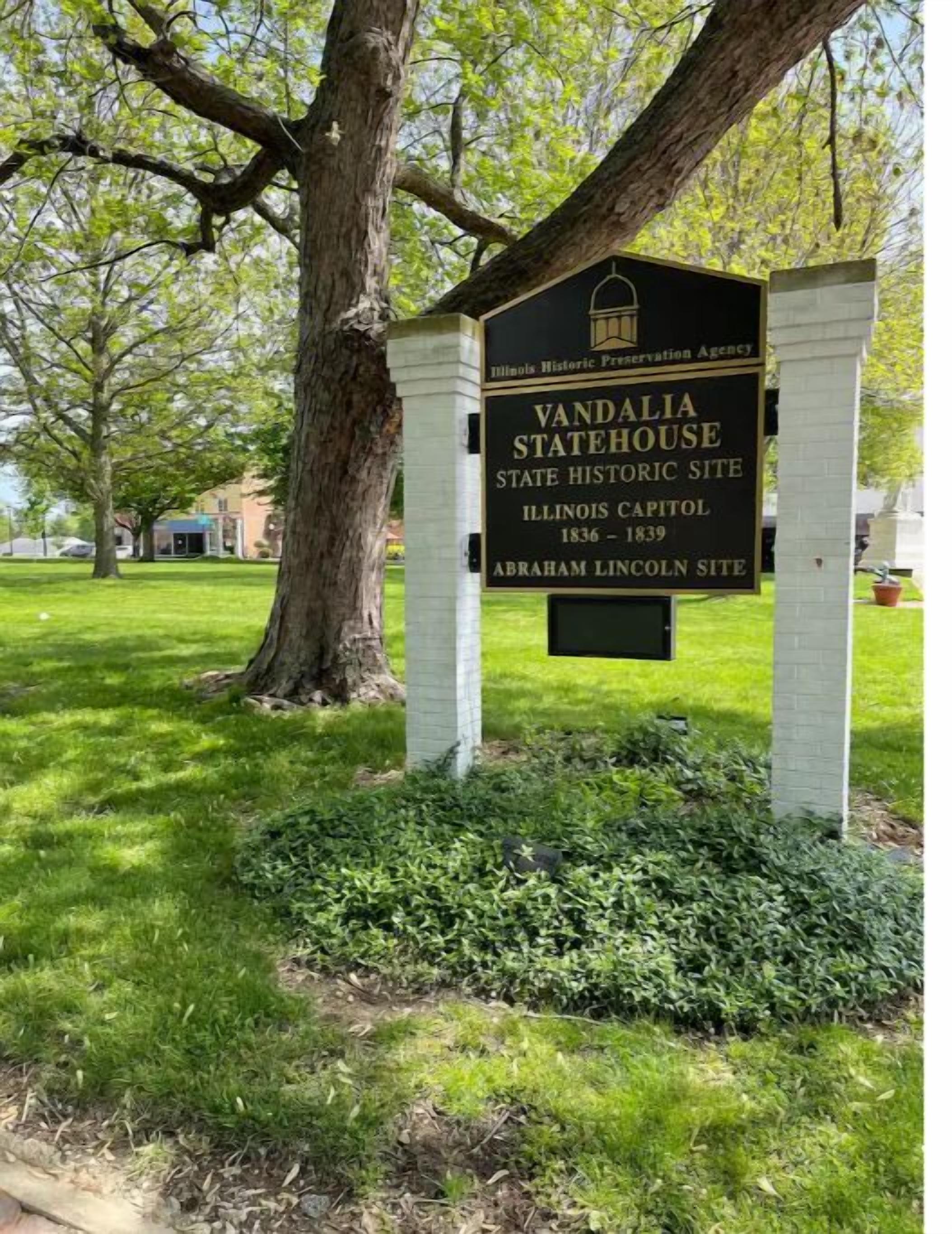 Placa indicando o Capitólio do Estado de Vandália, um local histórico em Illinois, com uma árvore grande e gramado em primeiro plano.