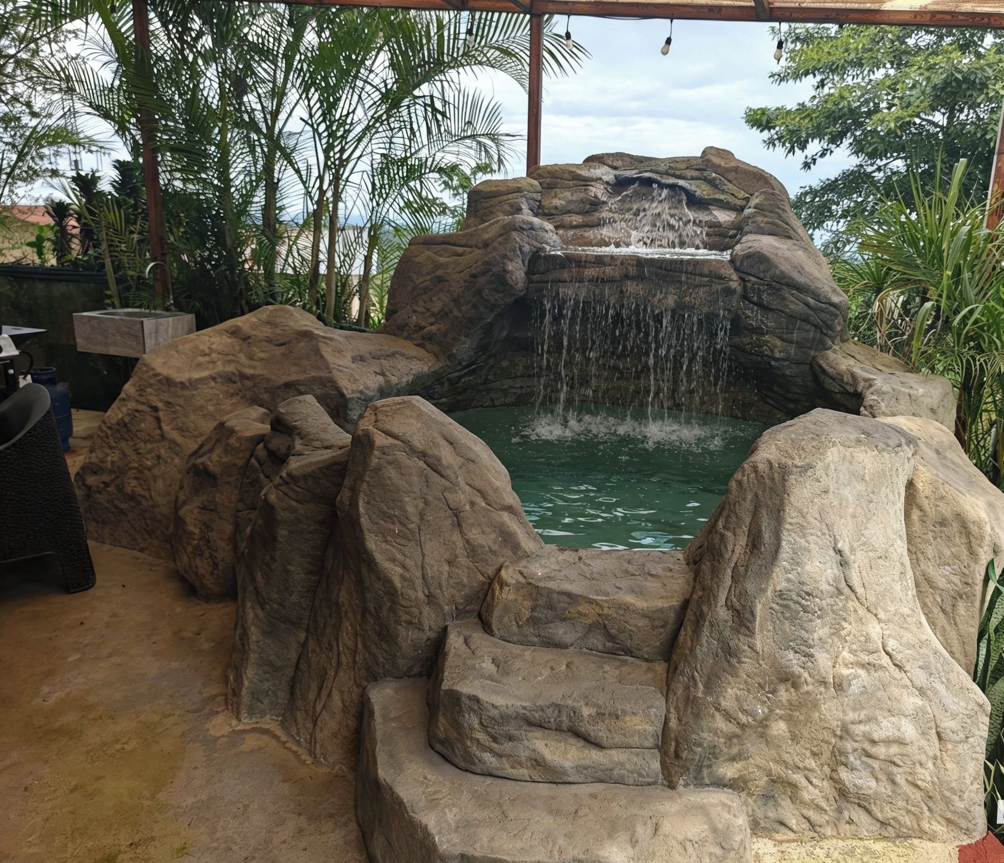 A rock formation with a waterfall and a pool, surrounded by palm trees.