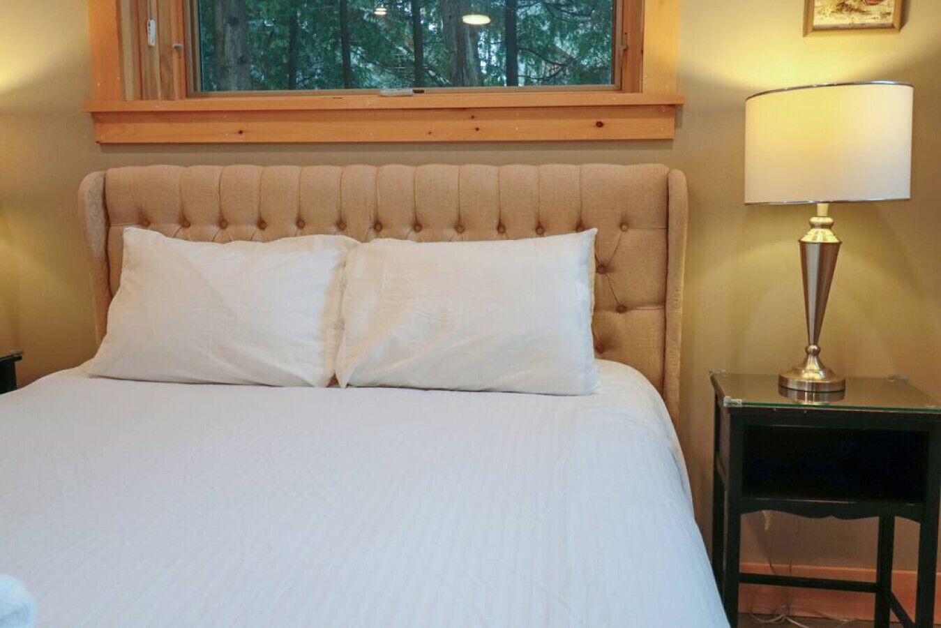 Ein Bett mit einer gebügelten Kopfstütze, zwei weiße Kissen und ein Nachttisch mit einer Lampe.
