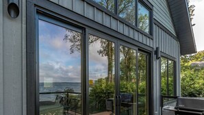 Ett modernt hus med stora glasdörrar som leder ut till en uteplats med grill och sittplatser.