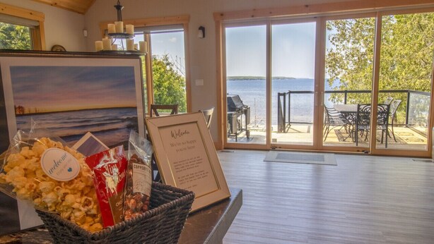 Ett välkomstområde med utsikt över sjön, en inramad välkomstskylt och en korg med snacks.
