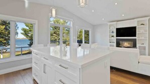 A modern kitchen with a large island, white cabinetry, and a fireplace. - Modern Waterfront Home on Georgian Bay w/ Hot Tub! (Victoria Harbour)