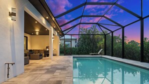 Un espace piscine extérieur moderne doté d’un toit en verre, d’un sol en pierre et offrant une vue sur la végétation environnante.