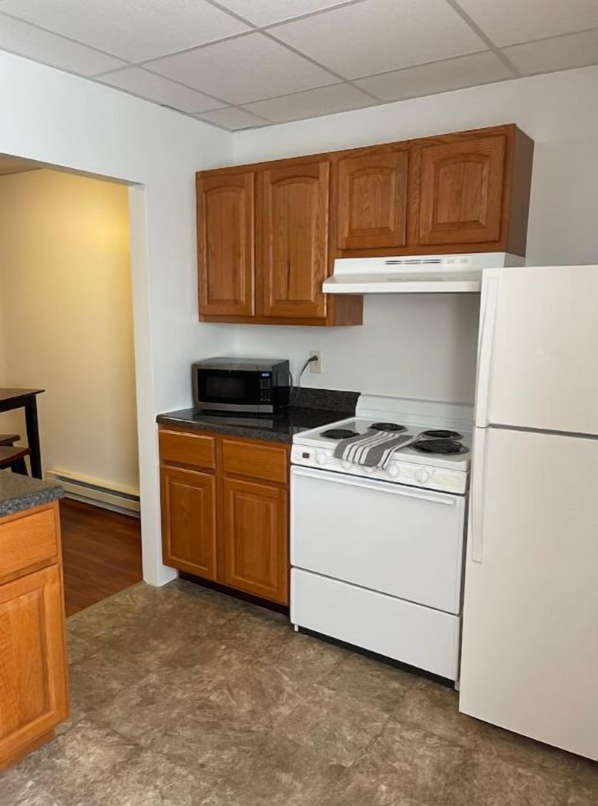 A small kitchen with wooden cabinets, a microwave, a stove, and a refrigerator.