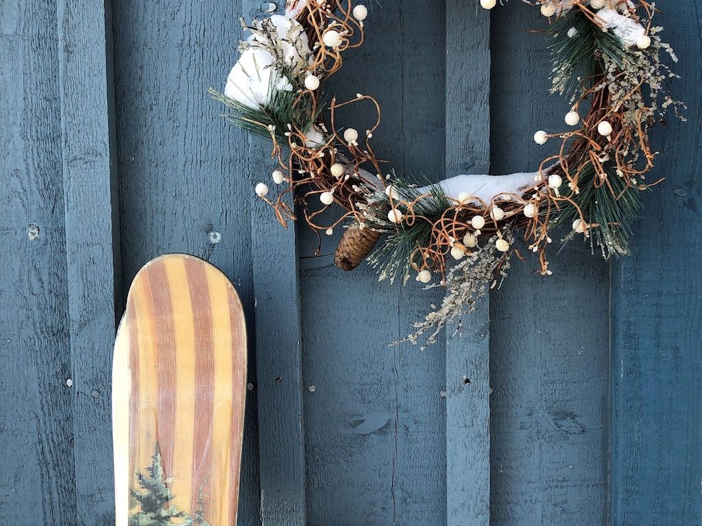 Eine Holzwand mit einem Schneeflocken-Kranz und einem Snowboard, das dagegen lehnt.