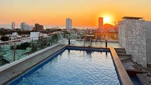 Una piscina en la azotea con vistas a la puesta de sol y al paisaje urbano.