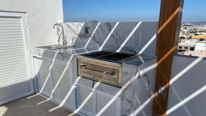 Una parrilla en la azotea con fachada de mármol, una puerta corrediza y vistas de la ciudad.