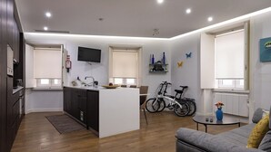 Un appartement moderne comprenant une cuisine, un coin repas et un salon. Il est doté d’un îlot central, d’un téléviseur fixé au mur et d’un vélo placé dans un coin.
