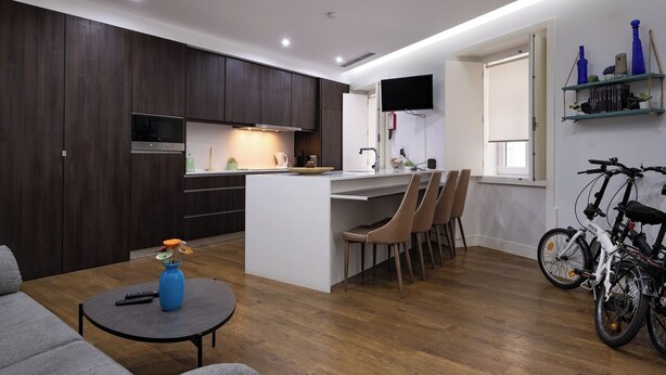 Une cuisine moderne avec des meubles en bois foncé, un îlot central doté de chaises, un coin repas avec une table ronde, et un vélo garé près de la fenêtre.
