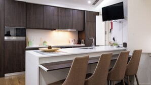 Une cuisine moderne avec des meubles en bois foncé, un plan de travail blanc, un four encastré et un téléviseur à écran plat fixé au mur.