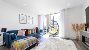 Una sala de estar moderna con un sofá azul, un tapete blanco mullido y un sillón colgante junto a un ventanal grande.
