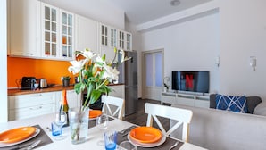 Een moderne keuken met witte kastjes, een eethoek met oranje borden en een woonkamer met een televisie.