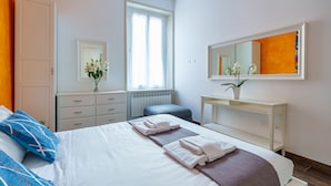 Een hotelkamer met een bed, een kaptafel, een spiegel, een raam en een plant in pot.