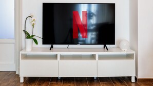 Een flatscreen televisie op een witte tv-meubel met een potorkidee.