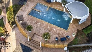 Una piscina esterna con una vasca idromassaggio a incasso, circondata da un solarium in pietra e poltrone relax.